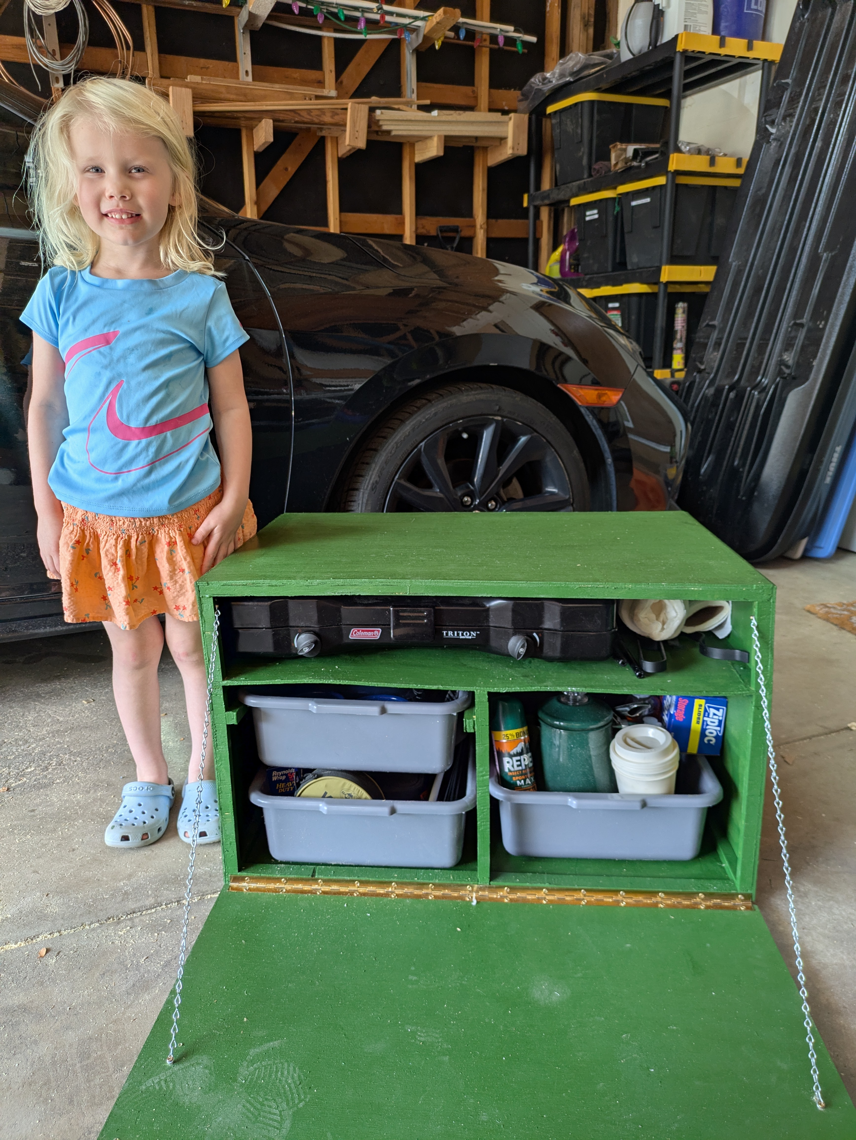 A green chuck box with camping items stored inside.